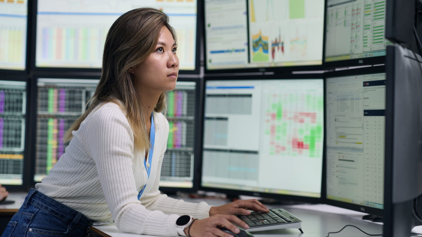 Person typing at a workstation with multiple monitors showing charts, tables, and a heatmap-style dashboard