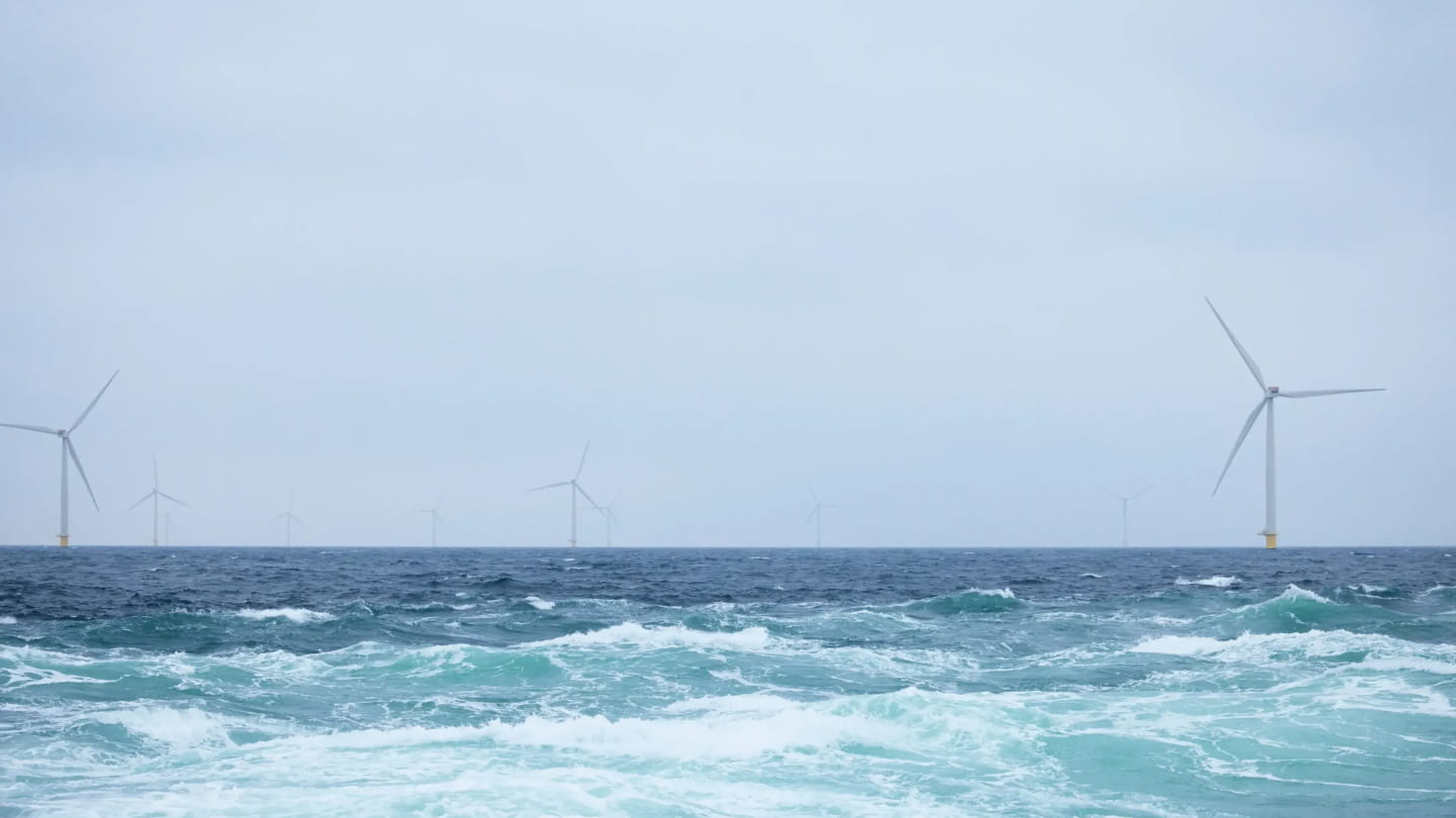 Waves in the foreground and a row of offshore wind turbines in the distance