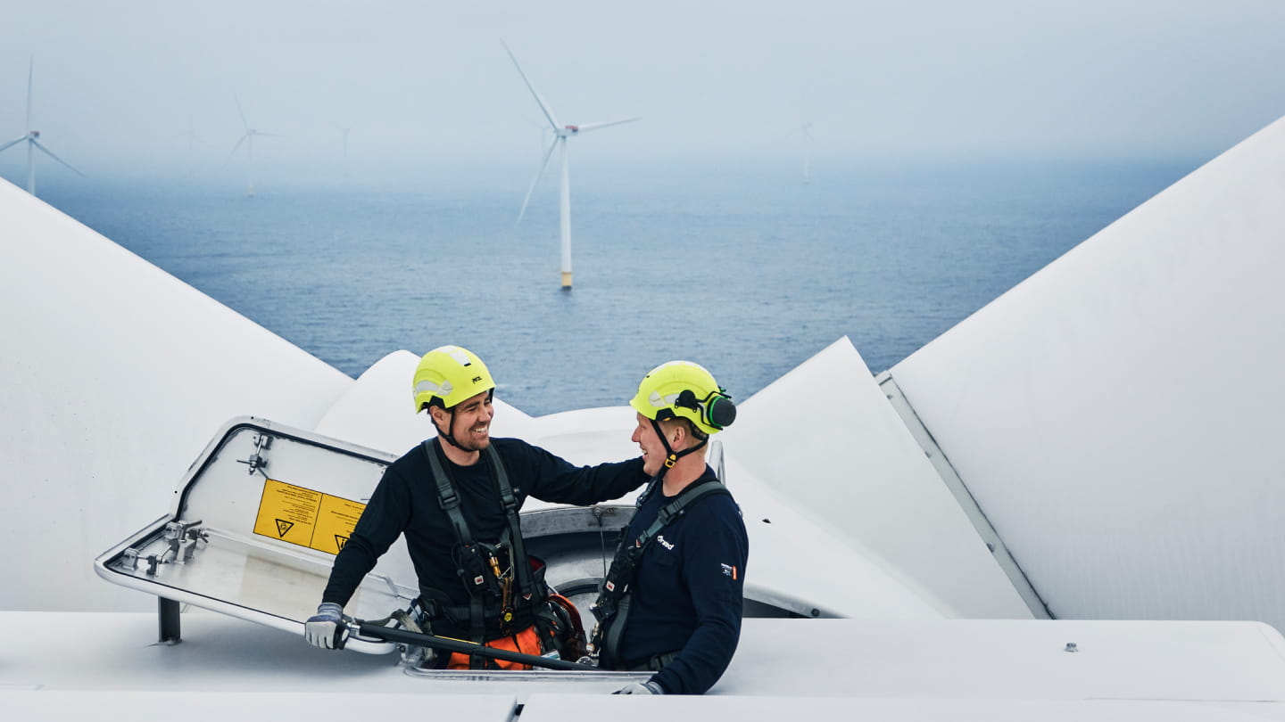 Two wind turbine technicians in safety helmets and harnesses standing on top of an offshore turbine