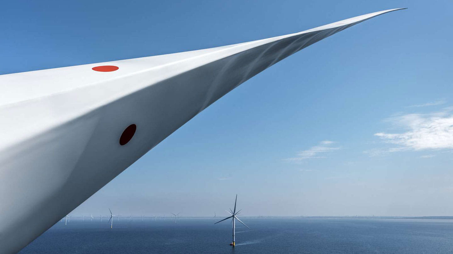Close-up of a wind turbine blade at sea, with other wind turbines visible in the background.