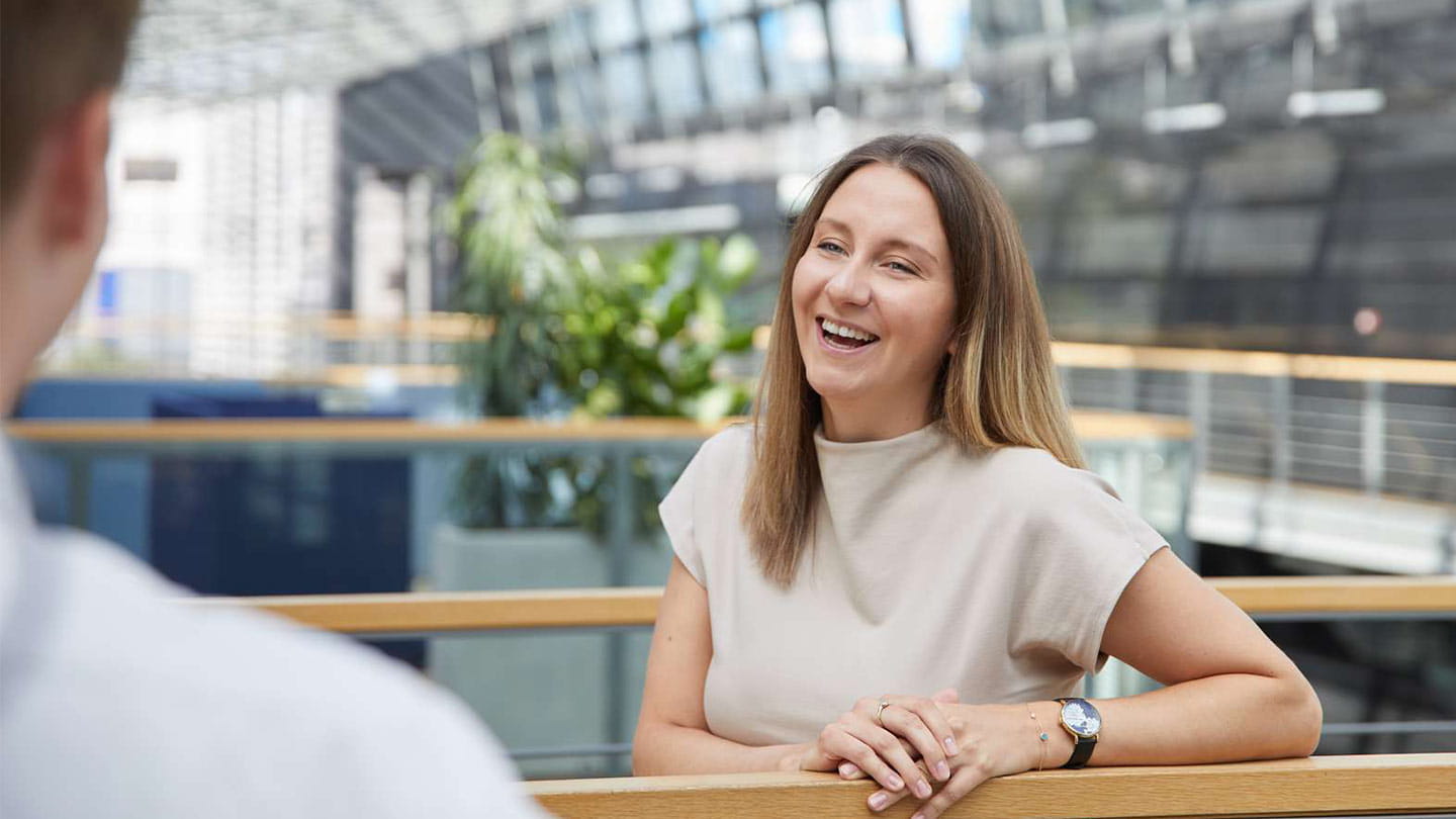 Smiling woman with a colleague in a modern office atrium, discussing offshore wind project opportunities.