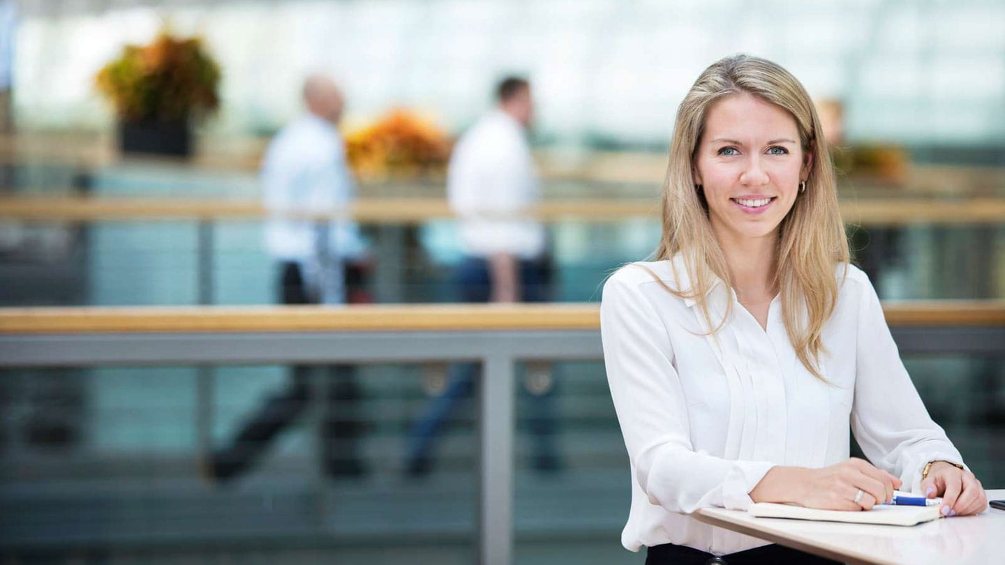 Ørsted employee with a white blouse and they hair down standing at a table with a notepad in front of her. 