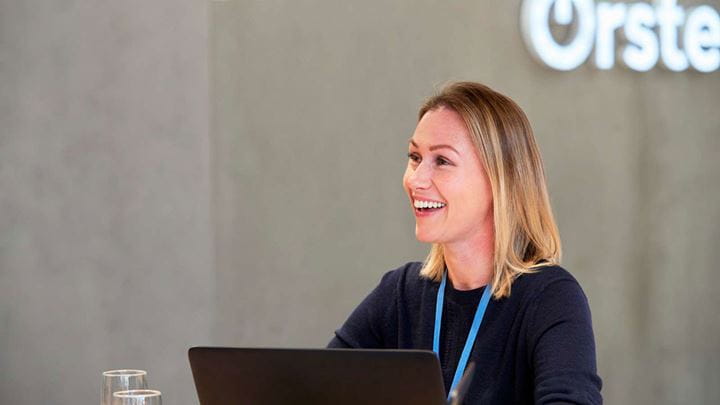 En medarbejder, der sidder ved sin arbejdsplads med en grå bluse på og høretelefoner.