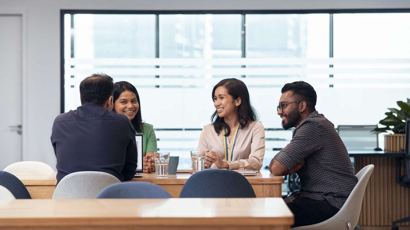 Employees engaged in a collaborative meeting around a table in a modern office environment.