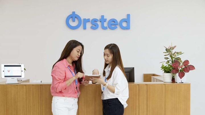 A man and a woman sitting on a blue circular sofa while engaging in conversation.