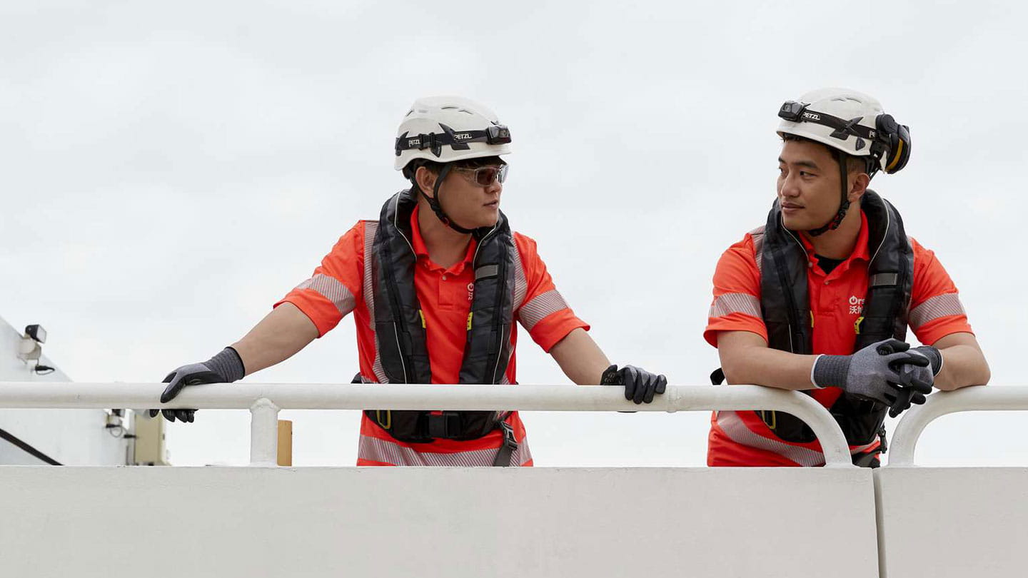 Orsted offshore technicians in PPE stand on a vessel deck, coordinating wind farm operations.