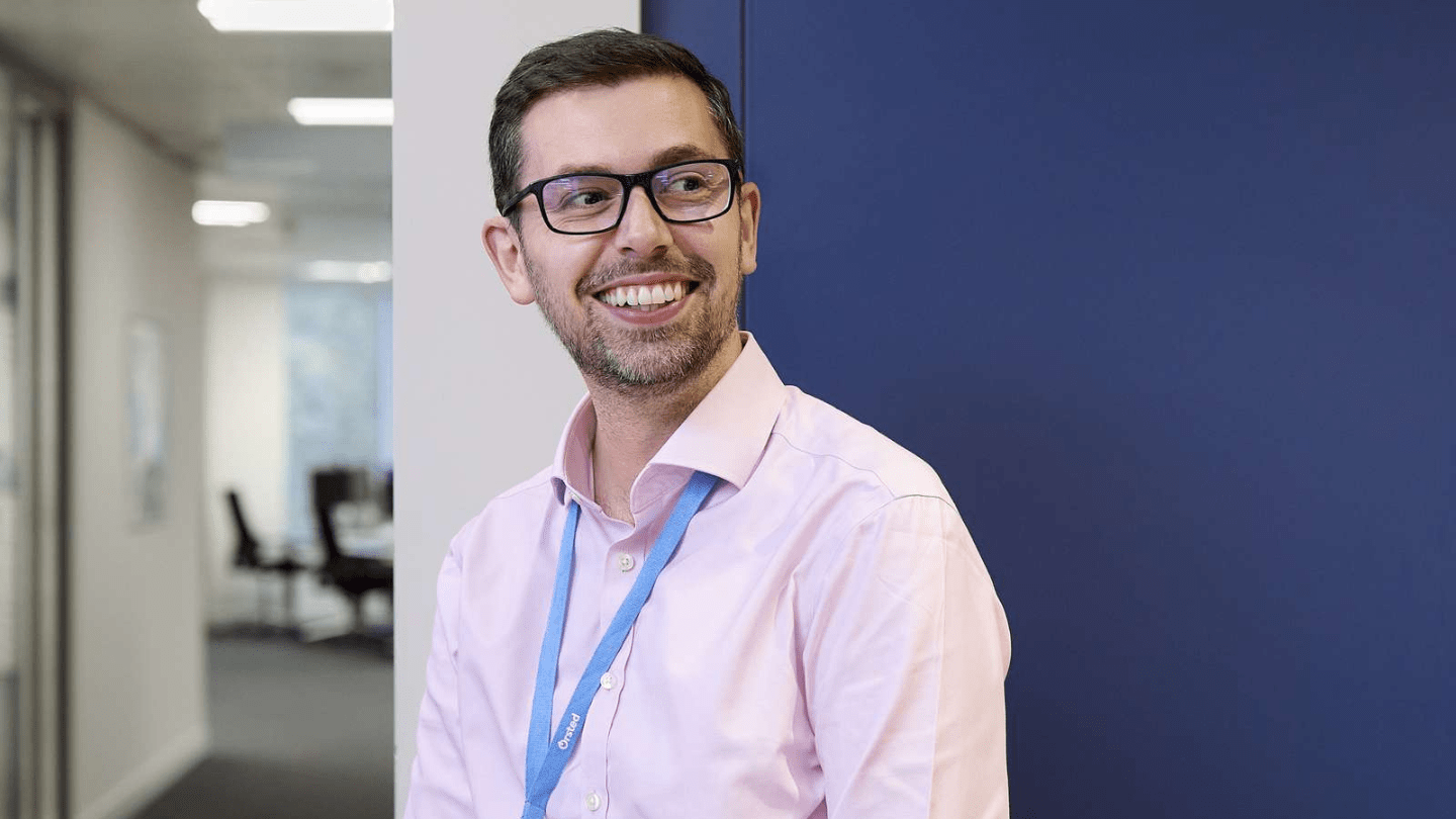 Portraits of employee in London Office. Standing in a hallway by a blue wall, smiling