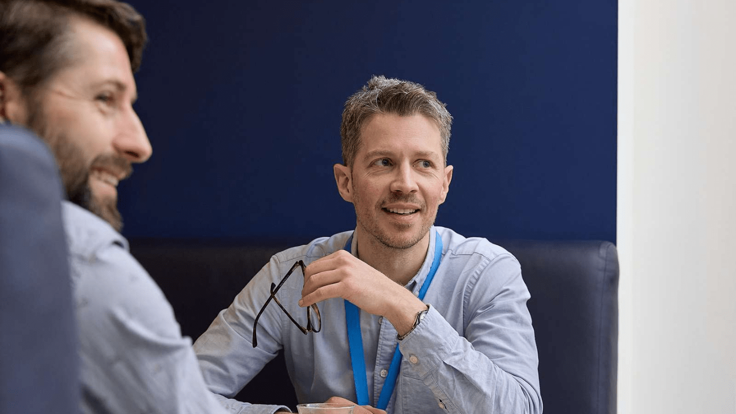 Portraits of employees in London Office. Sitting at a table, smiling, talking, dark blue wall