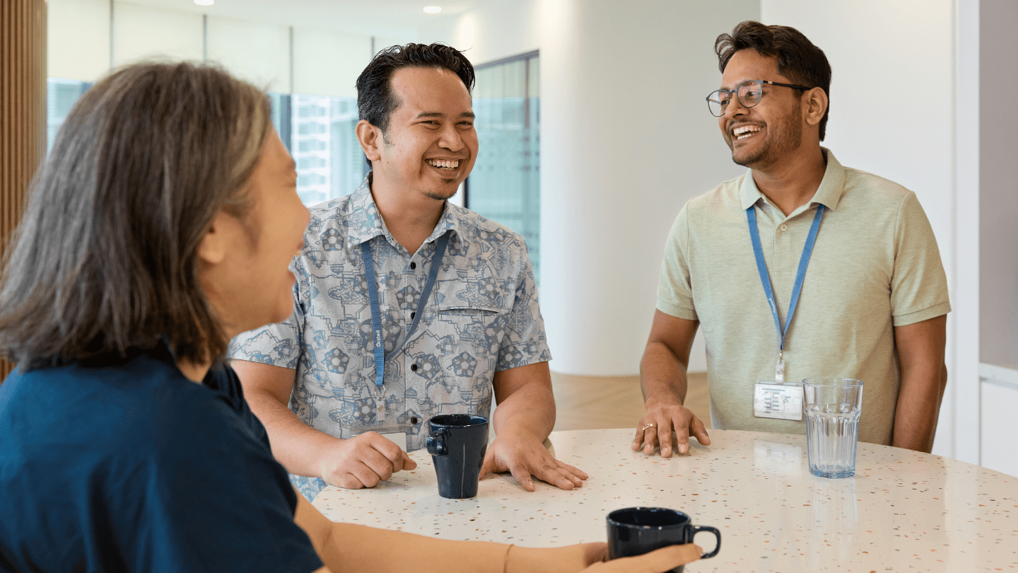 Employees around the table having a coffee chat, smiling. Kuala Lumpur office.