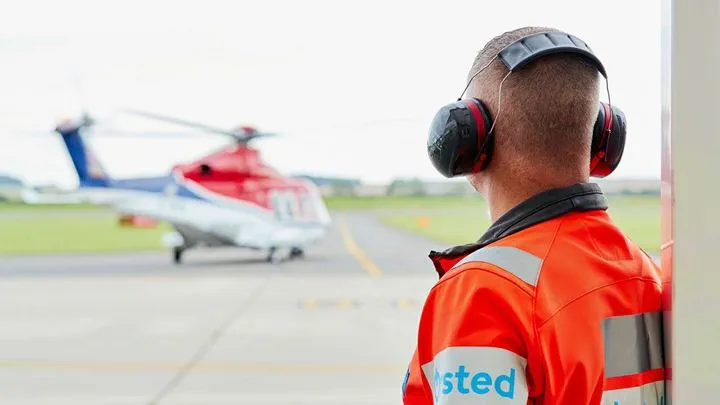 An Ørsted employee wearing protective gear watches on at a helicopter in the distance.