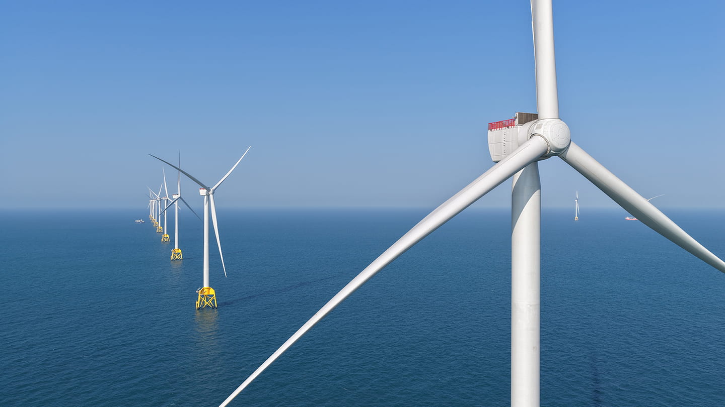Close-up of an offshore wind turbine and a row of turbines on yellow jacket foundations extends across sea