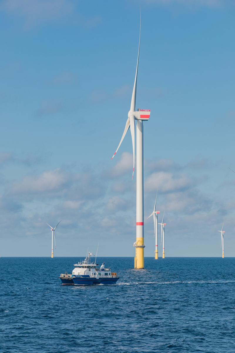 Offshore wind turbine with a service vessel in the foreground on a sunny calm day.