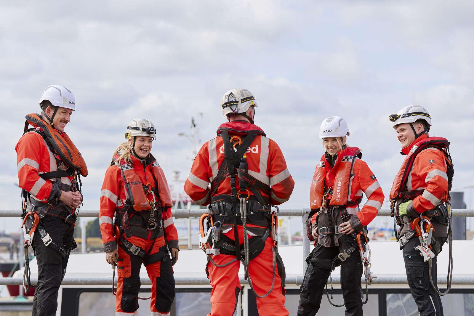 Offshore wind warm technicians standing in a circle with a sea vessel in the background