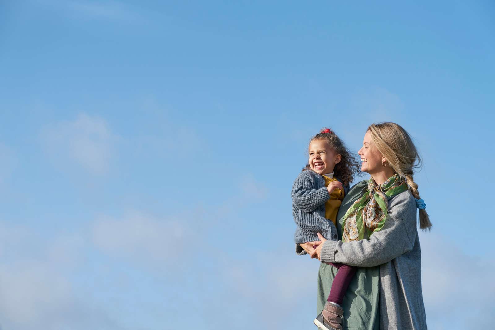 Mother with daughter in arms walking along the shoreline with sea in background