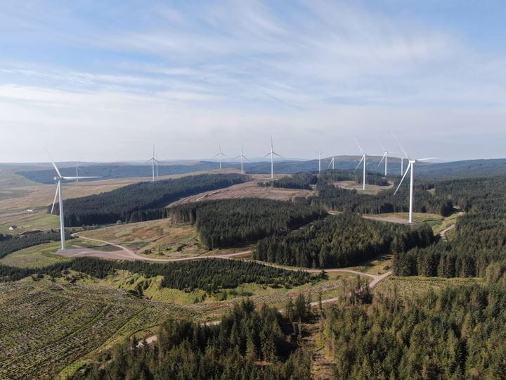 View of an onshore wind farm in a hilly grass and woodland area area