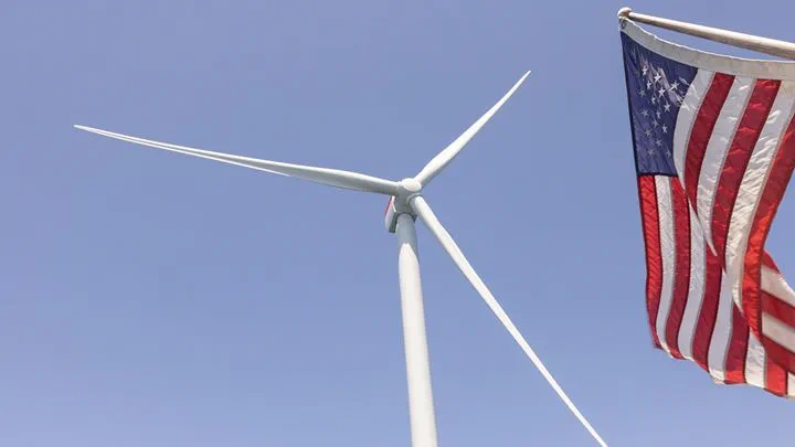 Wind turbine against a clear blue sky with an American flag waving in the foreground