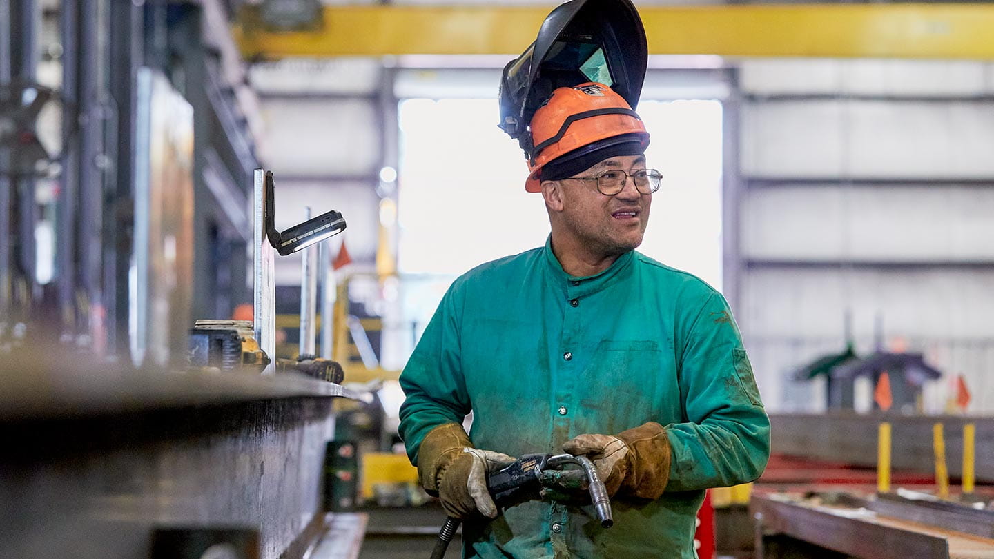 A welder wearing safety gear in a manufacturing workshop, showing Ørsted's impact on jobs, supply chain, and investment.